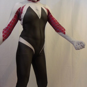 Puede incluir: Un traje de spandex blanco y negro con un dise&ntilde;o de telara&ntilde;a roja y blanca en los brazos. El traje tiene una m&aacute;scara blanca con capucha y un dise&ntilde;o de telara&ntilde;a negra.