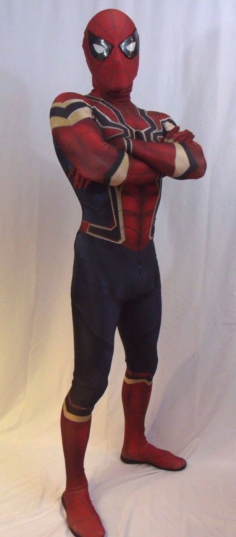 May include: A red and blue spandex costume with a spider web design. The costume includes a mask with a black eye piece and a white spider web design. The costume is worn by a person with arms crossed.