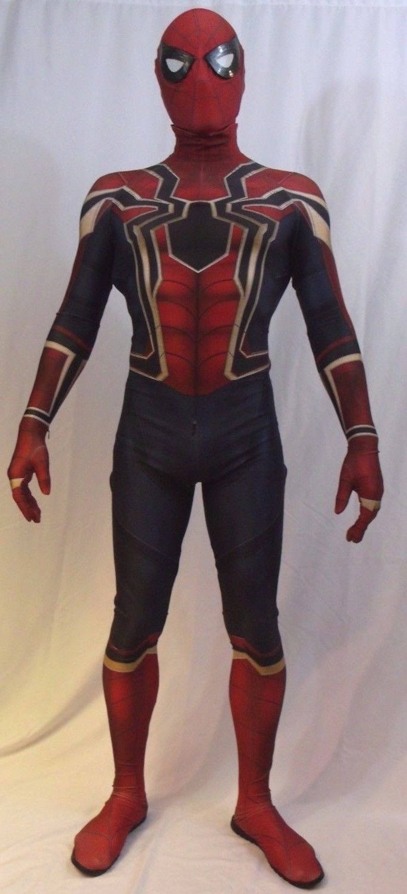 May include: A red and blue spandex costume with a spider web design. The costume has a black mask with a white spider logo. The costume is worn by a person standing on a white background.