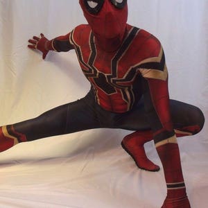 May include: A red and black spandex superhero costume with a spider design. The costume has a mask with black eye holes and a white spider design.