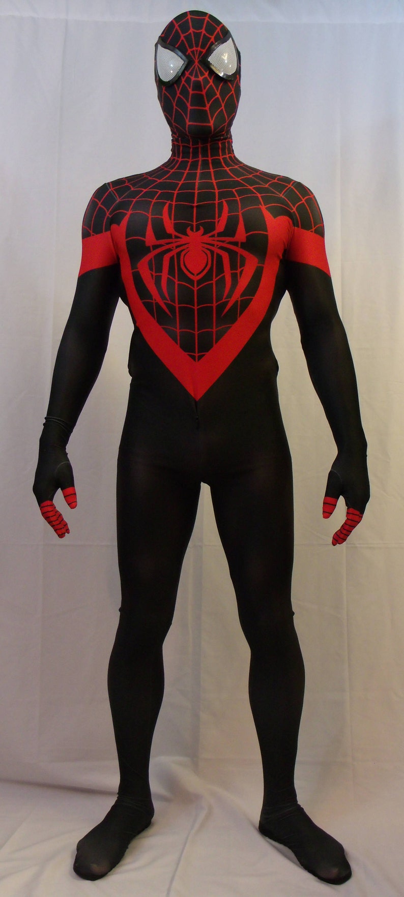 May include: A black and red spandex costume with a spider design on the chest. The costume has a black mask with a red spider design.