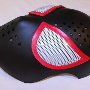May include: Black plastic mask with red and white spider-man inspired design. The mask has a mesh covering the eyes and a series of small holes around the nose and mouth.