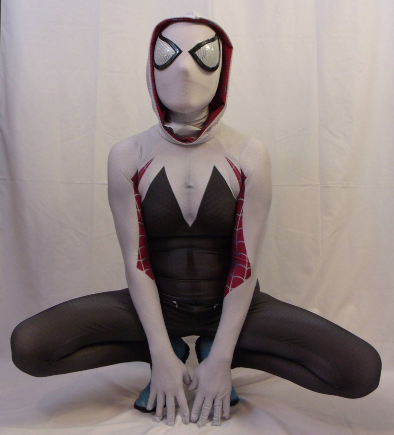 Puede incluir: Un traje de spandex blanco y rojo con una m&aacute;scara blanca y un dise&ntilde;o de ara&ntilde;a blanco y negro en los brazos. El traje lo lleva una persona en posici&oacute;n de cuclillas.