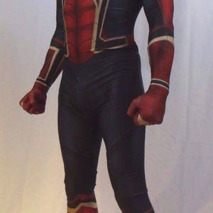 May include: A red and black spandex costume with a spider design. The costume has a mask with a red and black design and white eyes. The costume is worn by a person standing on a white surface.