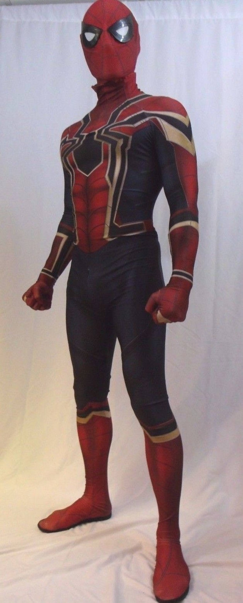 May include: A red and black spandex costume with a spider design. The costume has a mask with a red and black design and white eyes. The costume is worn by a person standing on a white surface.