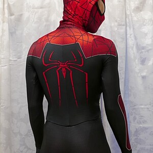 Puede incluir: Un traje de spandex negro y rojo con un logotipo de ara&ntilde;a rojo en la espalda. El traje tiene una capucha roja con un logotipo de ara&ntilde;a negro en la parte delantera.
