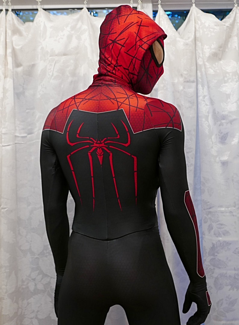 Puede incluir: Un traje de spandex negro y rojo con un logotipo de ara&ntilde;a rojo en la espalda. El traje tiene una capucha roja con un logotipo de ara&ntilde;a negro en la parte delantera.