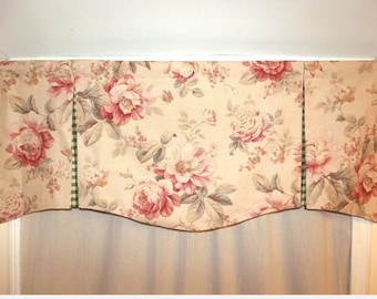 May include: A beige valance with a floral pattern featuring pink roses and green leaves. The valance has a green and white checkered trim along the sides.