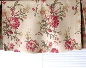 May include: A cream-colored valance with a floral pattern featuring red and green flowers. The valance has pleats and is hung over a window with white blinds.