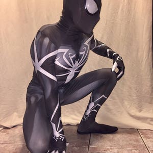 Może przedstawiać: Czarno-biały kostium z spandexu z wzorem pająka. Kostium ma czarną maskę z białym wzorem oka.