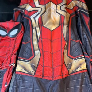 May include: A red and black Spiderman costume with a gold spider symbol on the chest. The costume has a zipper at the back.