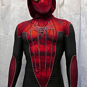 Puede incluir: Un traje de spandex rojo y negro con un dise&ntilde;o de telara&ntilde;a en el pecho. El traje tiene una capucha con una m&aacute;scara roja y negra.