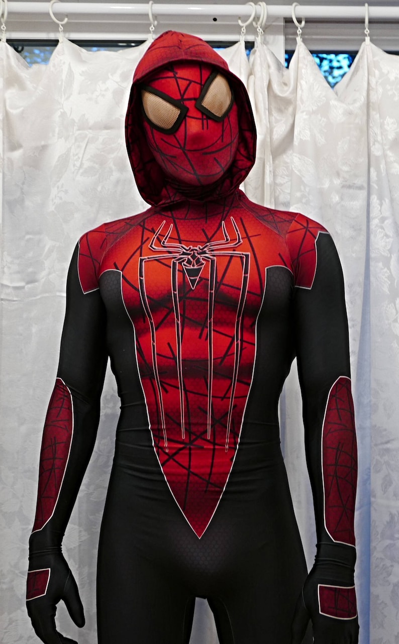 Puede incluir: Un traje de spandex rojo y negro con un dise&ntilde;o de telara&ntilde;a en el pecho. El traje tiene una capucha con una m&aacute;scara roja y negra.