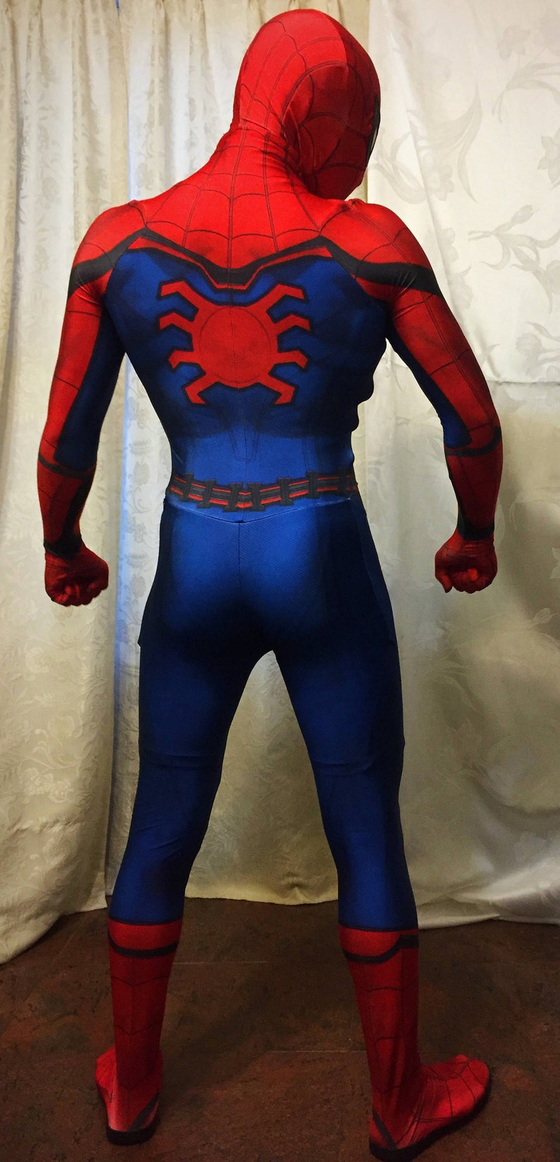 May include: A red and blue spandex costume with a spider design on the back. The costume has a black belt and red boots.