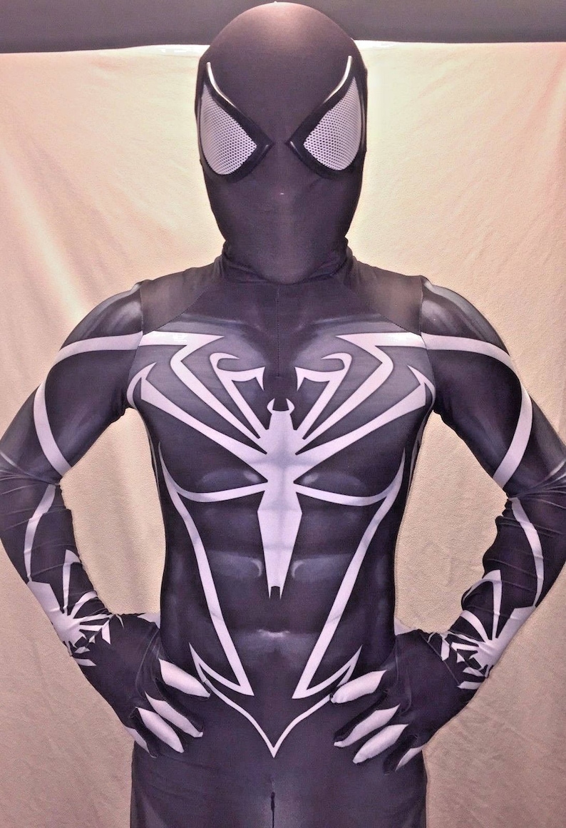 Może przedstawiać: Czarno-biały kostium z elastycznego materiału z wzorem pajęczyny na klatce piersiowej i ramionach. Kostium ma czarną maskę z białymi siatkowymi oczami.