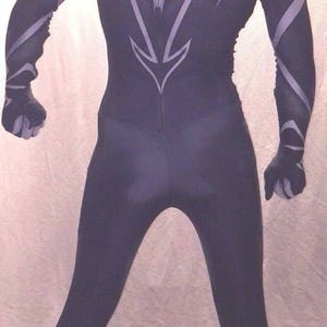 Może przedstawiać: Czarno-biały kombinezon z elastycznego materiału z wzorem pająka na plecach i nogach. Kombinezon ma czarną maskę z białym wzorem pająka.