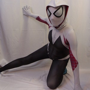 Puede incluir: Un traje de spandex blanco y negro con una m&aacute;scara con capucha blanca que presenta un dise&ntilde;o de telara&ntilde;a roja. El traje tiene detalles de telara&ntilde;a roja y blanca en los brazos y las piernas.