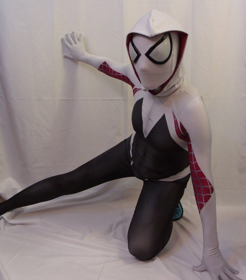 Puede incluir: Un traje de spandex blanco y negro con una m&aacute;scara con capucha blanca que presenta un dise&ntilde;o de telara&ntilde;a roja. El traje tiene detalles de telara&ntilde;a roja y blanca en los brazos y las piernas.