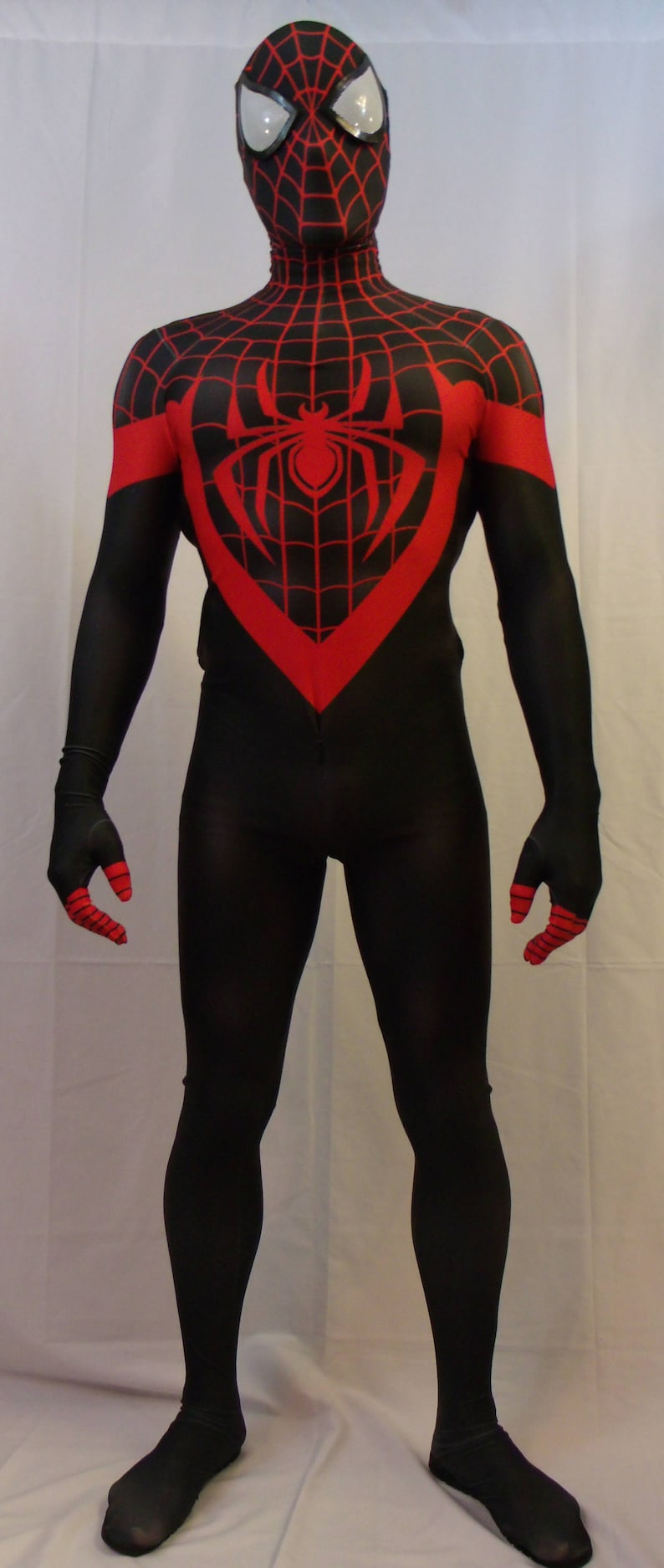 May include: A black and red spandex costume with a spider web design. The costume has a red spider symbol on the chest and red accents on the gloves and boots.