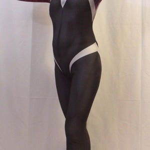 Puede incluir: Un traje de spandex blanco y negro con un dise&ntilde;o de telara&ntilde;a roja y blanca en los brazos y las piernas. El traje tiene una m&aacute;scara blanca con capucha y un dise&ntilde;o de ara&ntilde;a negro. La persona que lleva el traje est&aacute; de pie sobre una superficie blanca y lleva zapatos azules.