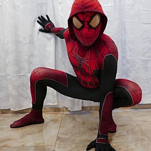 Puede incluir: Un disfraz de superh&eacute;roe rojo y negro con un dise&ntilde;o de telara&ntilde;a. El disfraz incluye una m&aacute;scara con capucha con un dise&ntilde;o de ara&ntilde;a roja.