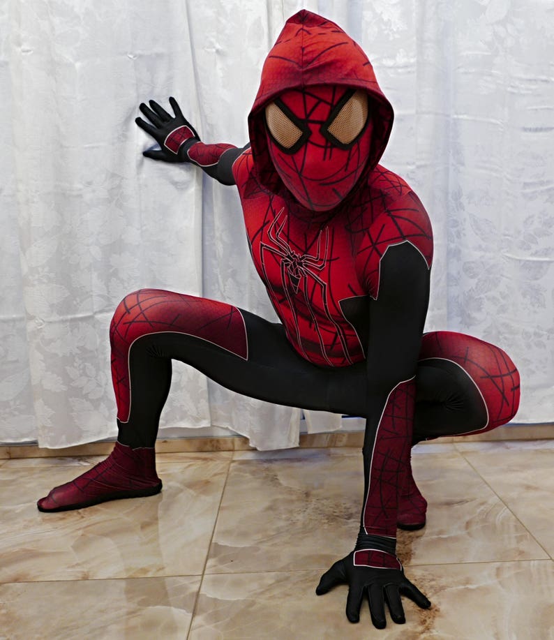 Puede incluir: Un disfraz de superh&eacute;roe rojo y negro con un dise&ntilde;o de telara&ntilde;a. El disfraz incluye una m&aacute;scara con capucha con un dise&ntilde;o de ara&ntilde;a roja.