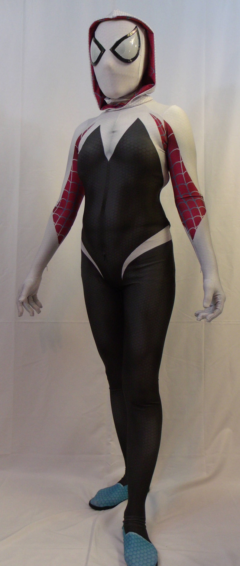 Puede incluir: Un disfraz de ara&ntilde;a blanco y rojo con una m&aacute;scara blanca y un mono negro. El disfraz tiene un s&iacute;mbolo de ara&ntilde;a blanco en el pecho y una telara&ntilde;a de ara&ntilde;a roja en los brazos. La persona que lleva el disfraz est&aacute; de pie sobre un fondo blanco.