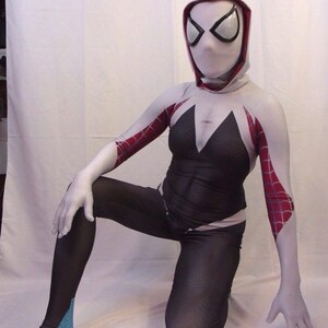 Puede incluir: Un traje de spandex blanco y negro con detalles de telara&ntilde;a roja. El traje incluye una m&aacute;scara con capucha blanca con ojos negros. La persona que lleva el traje est&aacute; arrodillada con una pierna doblada y la otra recta.
