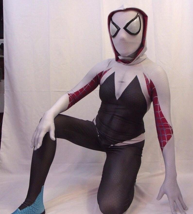 Puede incluir: Un traje de spandex blanco y negro con detalles de telara&ntilde;a roja. El traje incluye una m&aacute;scara con capucha blanca con ojos negros. La persona que lleva el traje est&aacute; arrodillada con una pierna doblada y la otra recta.