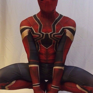 May include: A red and black spandex costume with a spider design. The costume has a red mask with black eyes and a white outline. The figure is in a crouching position with hands clasped in front.
