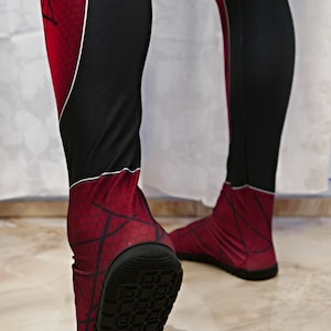 May include: A pair of red and black spandex leggings with a spiderweb pattern. The leggings have a black rubber sole on the bottom.
