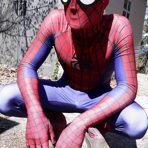 May include: A person dressed as Spider-Man in a red and blue costume with a black spider logo on the chest. The costume has a web pattern throughout. The person is crouching with their hands in front of them.