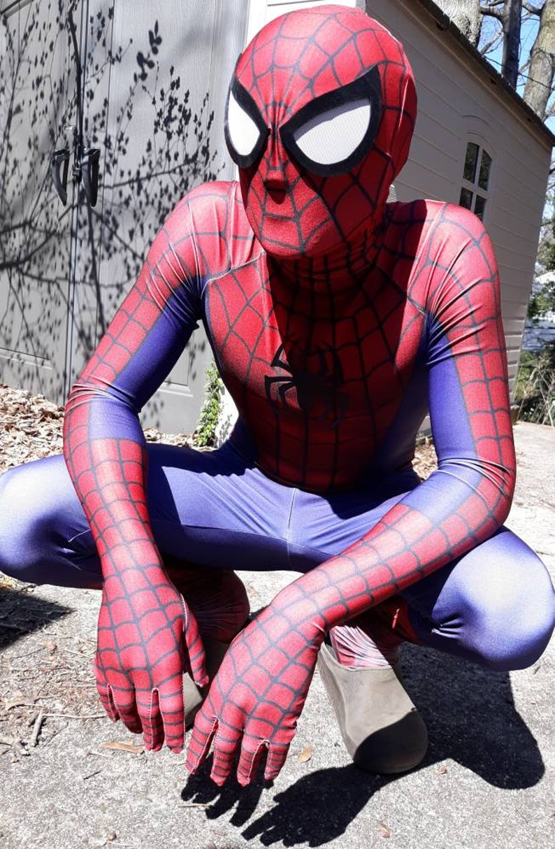 May include: A person dressed as Spider-Man in a red and blue costume with a black spider logo on the chest. The costume has a web pattern throughout. The person is crouching with their hands in front of them.