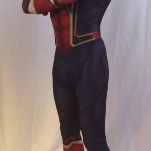 May include: A red and blue spandex costume with a spider design. The costume has a red mask with a white eye design. The costume is worn by a person standing on a white surface.