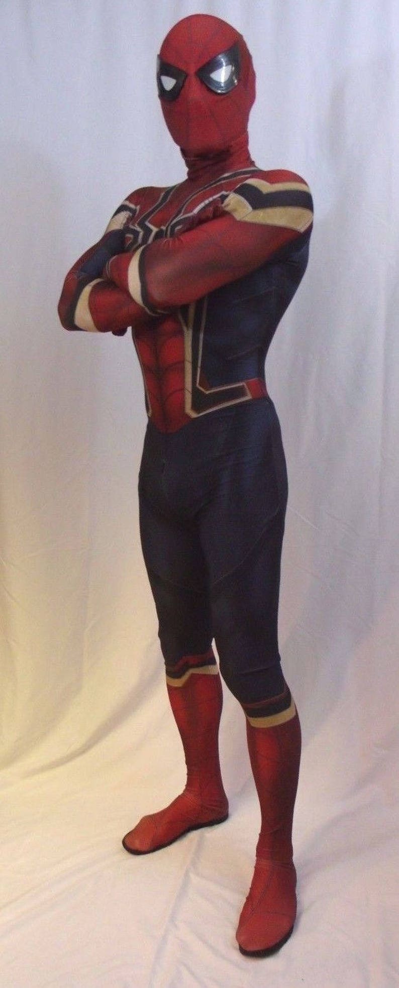 May include: A red and blue spandex costume with a spider design. The costume has a red mask with a white eye design. The costume is worn by a person standing on a white surface.
