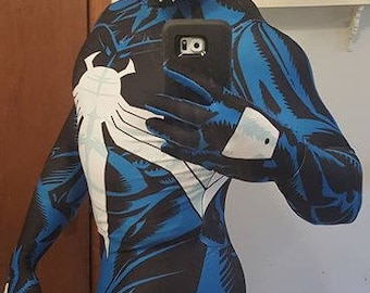 May include: A blue and black spandex bodysuit with a white spider-like design. The suit has a zipper in the back and a white symbol on the chest.