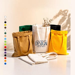 Könnte beinhalten: Eine Sammlung von Stofftaschen in verschiedenen Farben wie Beige, Grün, Schwarz, Gelb und Weiß. Die weiße Tasche trägt den blauen Schriftzug "YOUR DESIGN Put It Here!". Auf der linken Seite ist eine Spalte mit kleinen farbigen Kreisen zu sehen.