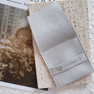 May include: A gray suede jewelry pouch with a diamond logo and the text "CARRIE.J" printed on the front.