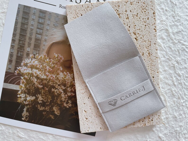 May include: A gray suede jewelry pouch with a diamond logo and the text "CARRIE.J" printed on the front.