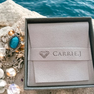 May include: A gray jewelry box with a light gray suede interior and the text "CARRIE.J" printed on the front.
