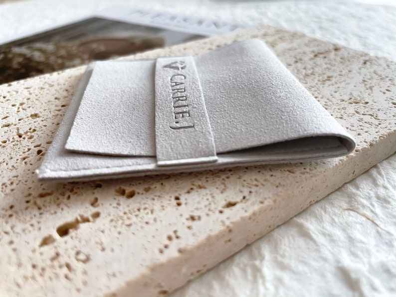 May include: A white, folded, rectangular pouch with the text "CARRIE J." embossed on the front.