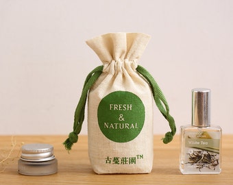 May include: A small white drawstring bag with green drawstrings and a green circle that says "FRESH & NATURAL" in white text. The bag is sitting on a wooden surface next to a clear glass bottle with a silver cap and a label that says "White Tea".