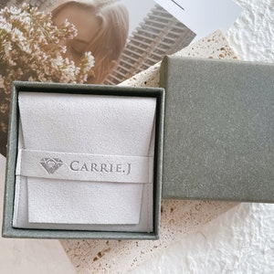 May include: A gray jewelry box with a white velvet interior. The box has a diamond logo and the text "CARRIE.J" on the inside.