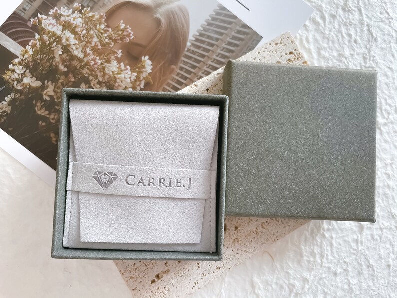May include: A gray jewelry box with a white velvet interior. The box has a diamond logo and the text "CARRIE.J" on the inside.