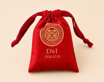May include: A red drawstring bag with a gold circular design and the initials "D&J" along with the date "2026.10.18" printed in gold. The bag is made of a soft material and has a matching red drawstring closure.