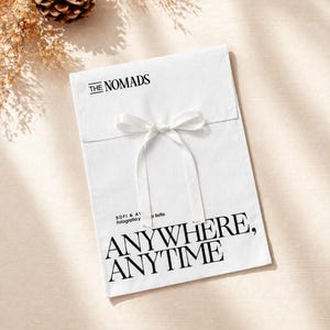 Könnte beinhalten: Eine weiße Verpackung, die mit einem weißen Band gebunden ist. Der Text "THE NOMADS" steht oben, darunter in großen, fetten Buchstaben "ANYWHERE, ANYTIME". Die Verpackung hat auch den Text "SOFI & A fotografia y Sofia".