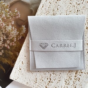 May include: A gray suede jewelry pouch with a diamond logo and the text "CARRIE.J" printed on the front.
