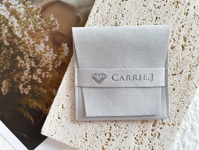 May include: A gray suede jewelry pouch with a diamond logo and the text "CARRIE.J" printed on the front.