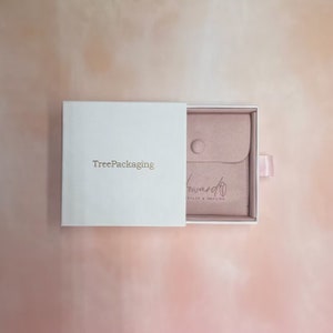 Puede incluir: Una caja blanca con el texto "TreePackaging" en la parte delantera. La caja est&aacute; abierta y revela una bolsa de terciopelo rosa con el texto "toward health & healing" en la parte delantera.