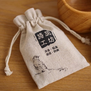 May include: A small, off-white drawstring bag made of natural fabric with black text that reads "香 促 工 坊" and "清香. 驱虫 避湿. 防霉". A small bird illustration is printed on the bag.